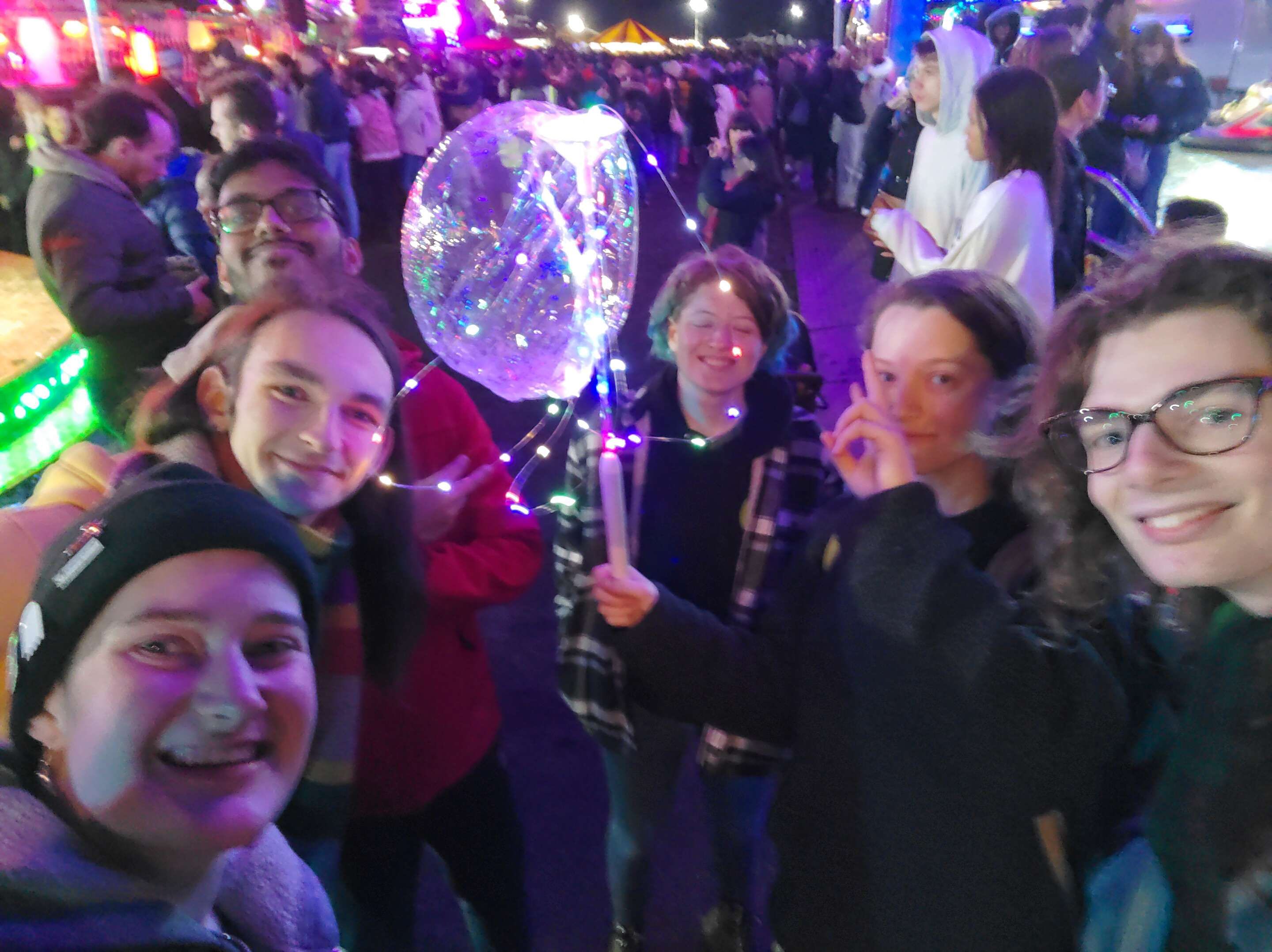 A group of people standing around a deflated clear balloon with fairy lights on it